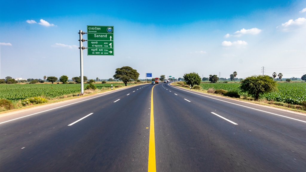 Modern highway leading to Sanand Gujarat through green agricultural fields under clear blue sky